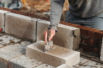 Builder cutting concrete block with chisel and hammer to right size