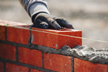 Bricklayer constructing stone wall using bricks, cement mortar mix and trowel