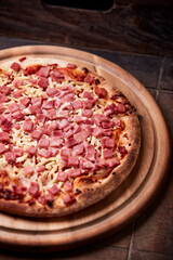 Pizza with ham and mozzarella cheese on wooden background. Soft focus. Close up	