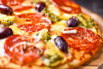 Pizza with chorizo ​​sausage, mozzarella and cheddar cheese, olive pesto and kalamata olives. Wooden background. Soft focus. Close up.	