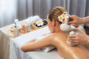 Hot herbal ball spa massage body treatment, masseur gently compresses herb bag on woman body....