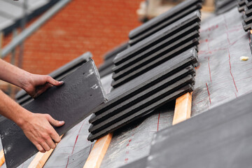 Roofing contractor carefully places slate roofing tiles on a structure's roof ensuring proper...