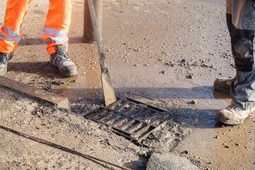 Builders opening blocked road gully for cleaning to prevent street flooding