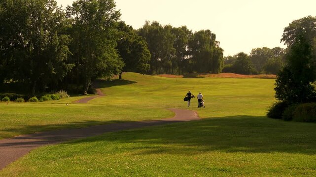 Golfers walking across a golf green with golf caddy