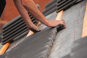 Skilled worker busy applying roofing material on sloped roof focused on securing elements for...