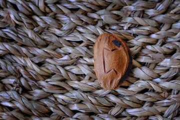 A single apricot pit with a carved rune rests on a textured straw mat. The minimalist composition...