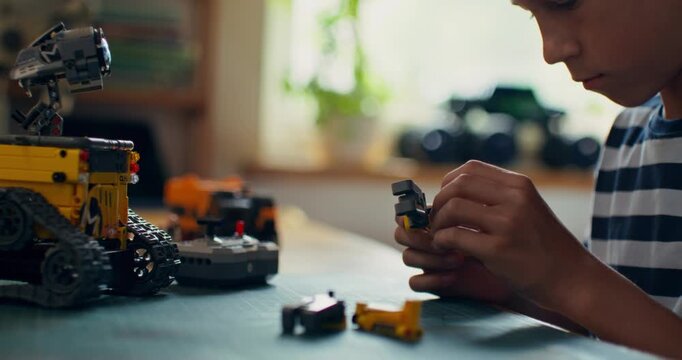 A boy builds a robot from a construction kit while sitting at a table at home. Close-up of his hands, unrecognizable person