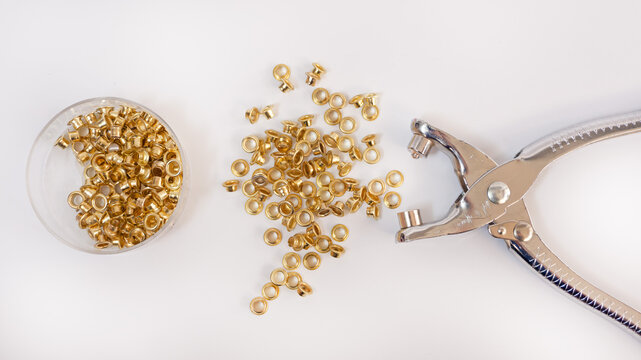 Remachadora manual plateada junto a remaches dorados dispersos sobre fondo blanco