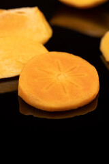 peeled ripe juicy persimmons ripe orange persimmons are reflected on the black mirror surface, closeup