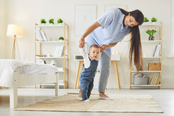 Childs first steps in learning to walk, mother holding hands of toddler with love, support and...