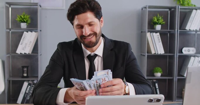 Happy rich man counting money cash, managing his finances, earned much money after having deal, dressed formally, posing in office room, having financial wealth. Profit and earnings concept