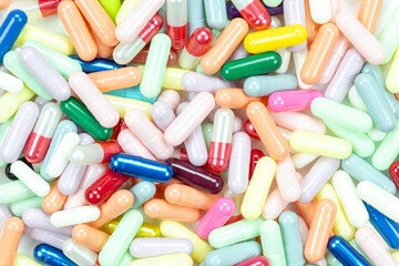 Top-down view of colorful medicine pills and capsules scattered as a background. A pharmaceutical...