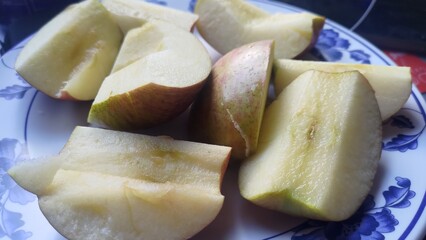 Close-up of fresh, juicy apple slices served on a decorative plate with a blue floral pattern. This image represents a healthy snack, nutritious diet, organic food, and a vegetarian lifestyle.