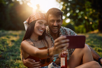 Happy couple of festival goers taking selfie while waiting for open air music concert.