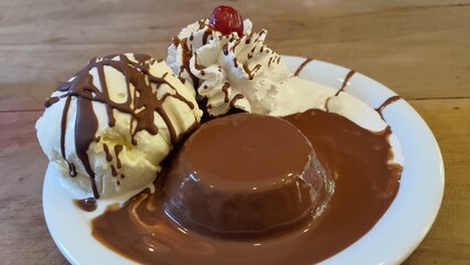 Close-up of an chocolate petit gateau dessert on a white plate with a scoop of vanilla ice cream, whipped cream drizzled with chocolate sauce and a maraschino cherry on top.