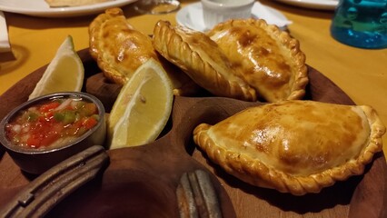 Close-up of traditional Argentinian baked empanadas served on a rustic wooden platter with fresh lemon wedges and a small bowl of chimichurri sauce, a typical South American appetizer.