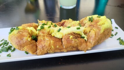 Close-up of a delicious homemade baguette stuffed or garlic bread and garnished with fresh chopped chives. A savory breakfast dish served on a white plate on a dark restaurant table.