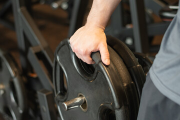 Muscular caucasian young man bodybuilder picking up heavy dumbbell at gym. Close up