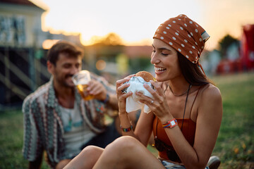 Happy festival goer eating hamburger during open air music concert in summer.
