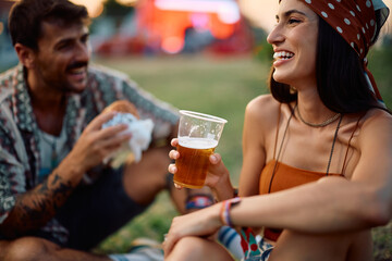 Happy woman drinking beer while attending summer music festival with her boyfriend.