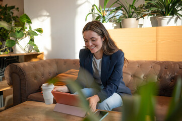 Smiling businesswoman using digital tablet and drinking coffee in modern office lounge