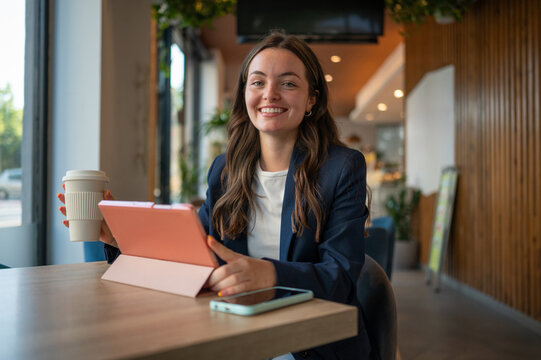 Businesswoman smiling and holding coffee while using tablet in cafe