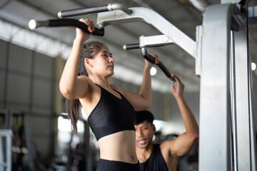 Trainer assisting female athlete with chin-ups in gym