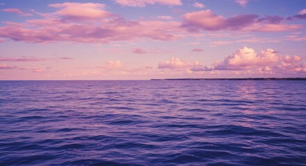 Peaceful seascape view with calm blue waters under a pastel pink and purple sky at sunset time.