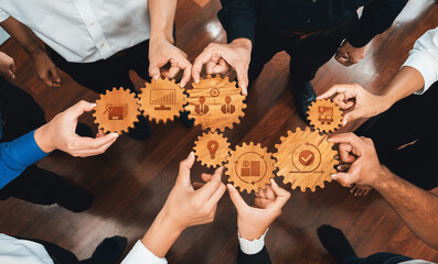 Aerial view of diverse hands holding wooden gears, symbolizing collaboration and teamwork in...