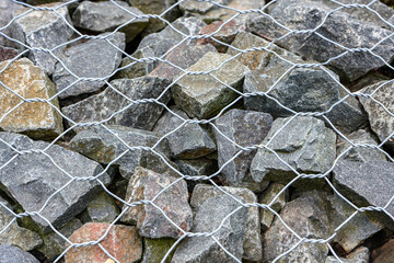 Close-up of metal wire mesh gabion filled with gray crushed stones, used for erosion control,...