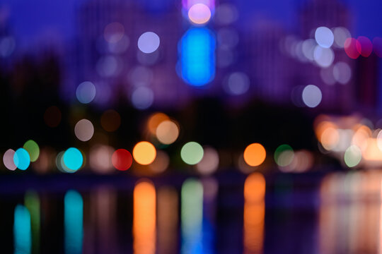 Colorful city lights bokeh at night with reflections on water, abstract defocused urban background with vibrant glowing circles, dreamy atmosphere and evening cityscape light blur