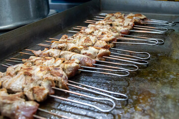 Juicy pieces of marinated meat are sizzling on skewers, cooking on a hot grill in a lively evening...