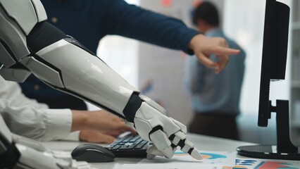 A futuristic robotic arm reaching towards a computer while human colleagues engage in discussion....