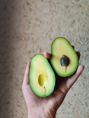 Fresh avocado halves in female hand on neutral background. Healthy eating concept.
