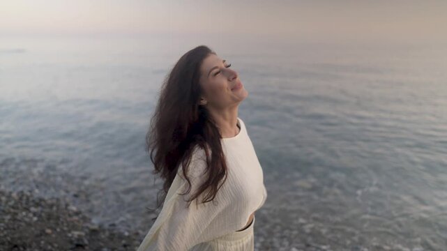 Woman breathing deeply, standing on sandy beach during golden hour, experiencing freedom and wellness, connecting with serene natural landscape
