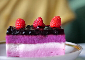 Exquisite Slice of Raspberry and Blueberry Layered Mousse Cake on a White Plate - Close-Up of Vibrant Purple and Pink Dessert Slice with Fresh Fruit Topping