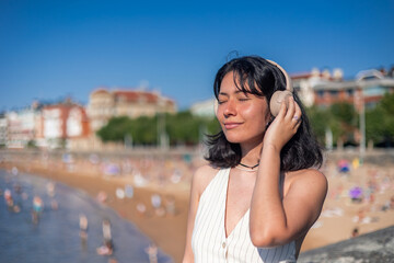 Young asian woman listening music with headphones enjoying summer near the beach