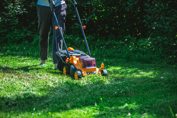 Yellow and black lawn mower cutting through fresh green grass in a vibrant garden on a sunny summer day, ensuring a beautifully maintained and healthy lawn