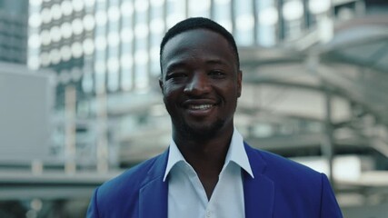 Portrait of African American male entrepreneur in formal wear smiles on city street. Corporate trainee man expresses positive emotion before new work day against office buildings