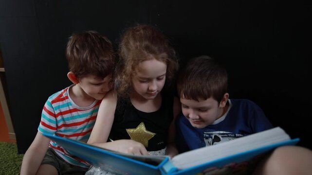 Sister and her brothers sitting on the floor and looking at photo album.