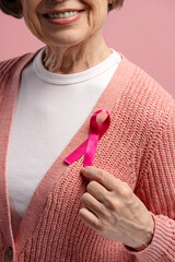Senior woman showing pink ribbon for breast cancer awareness, fighting against illness and...