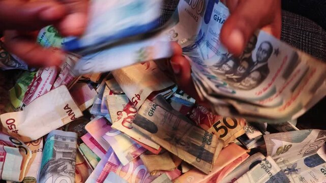 Black African person counting staightening unfolding arranging and counting Ghanaian cedi notes on desk. close up top view

