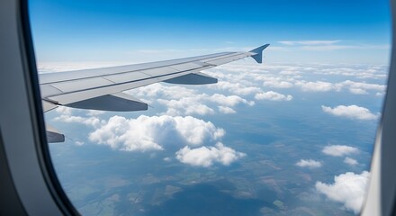 Obraz premium Airplane wing viewed from passenger window, soaring above fluffy clouds and distant land.