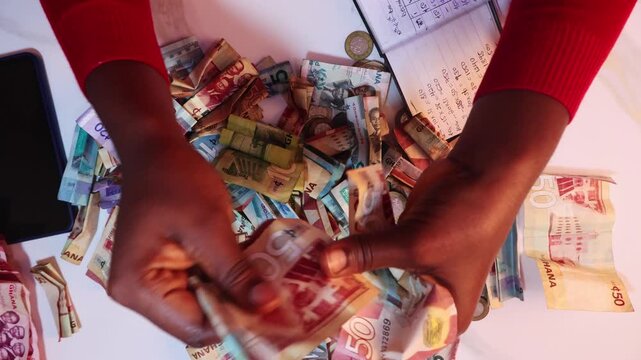 Black African person counting staightening unfolding arranging and counting Ghanaian cedi notes on desk. close up top view
