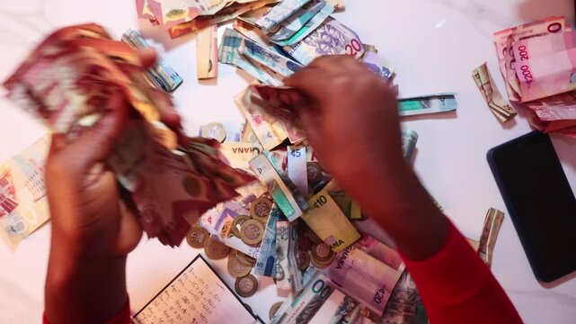 Black African person counting staightening unfolding arranging and counting Ghanaian cedi notes on desk. close up top view
