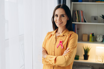 Beautiful smiling woman smiling with pink ribbon showing support for breast cancer awareness