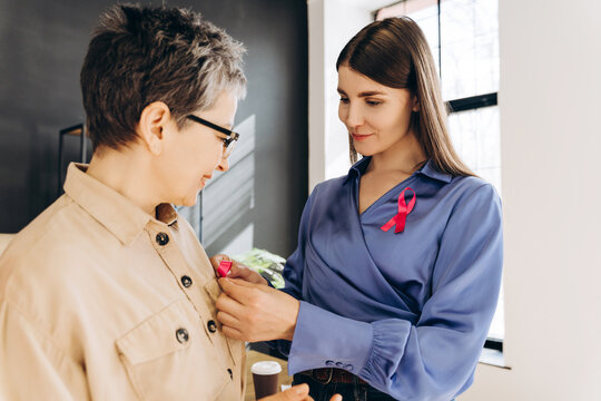 Woman attaching pink ribbon on colleague's shirt for breast cancer awareness month