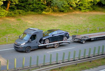 Damaged Black Car on Flatbed Tow Truck with Trailer – Roadside Recovery and Vehicle Transport on Highway