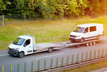 White Van on Flatbed Tow Truck Trailer Driving on Highway – Vehicle Transport and Logistics Concept