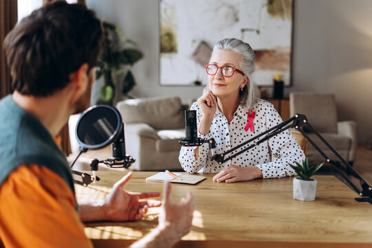 Radio host interviewing mature woman with pink ribbon about breast cancer awareness